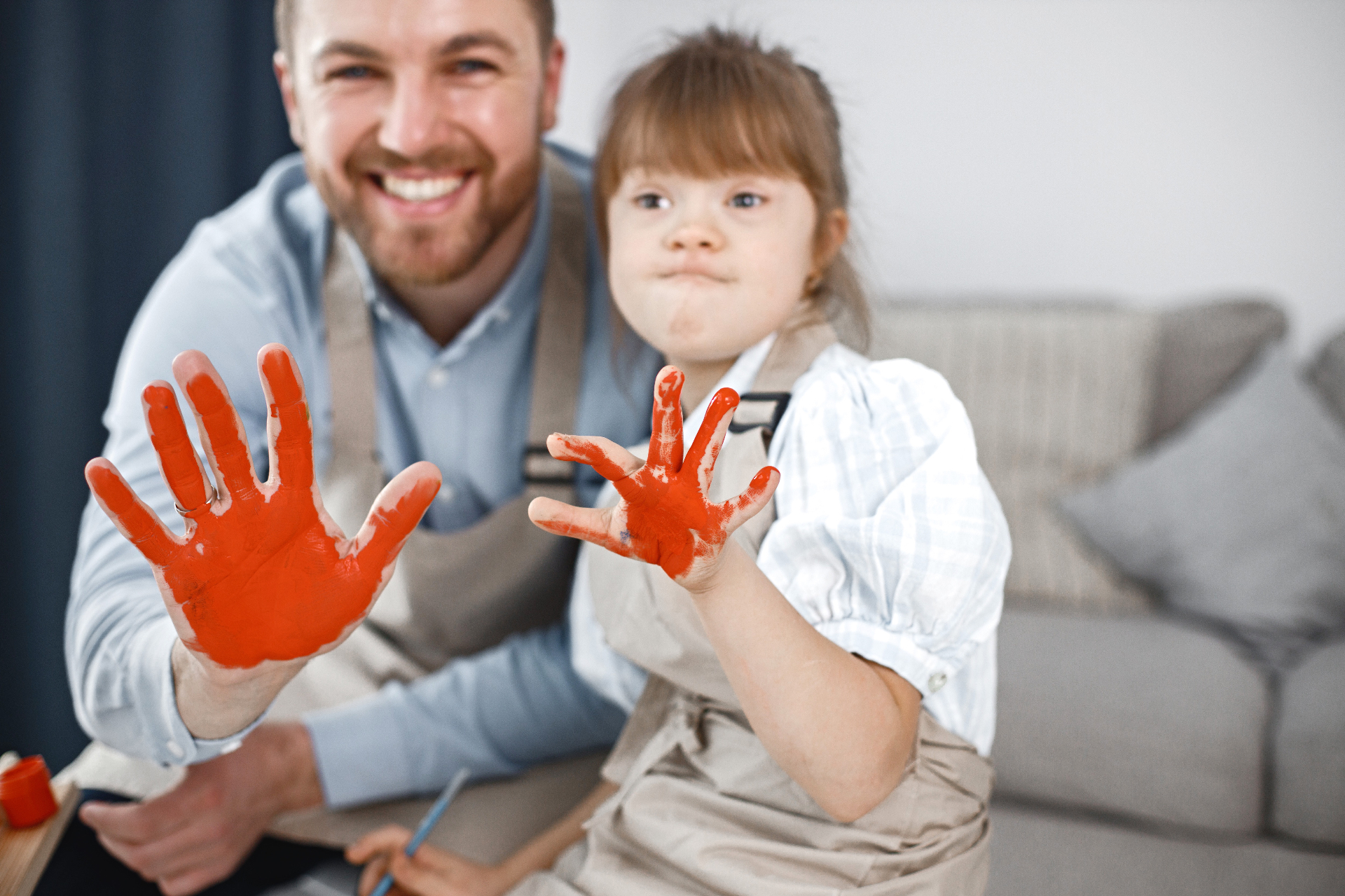 A father and his daughter with Down syndrome smiling and showing painted hands together